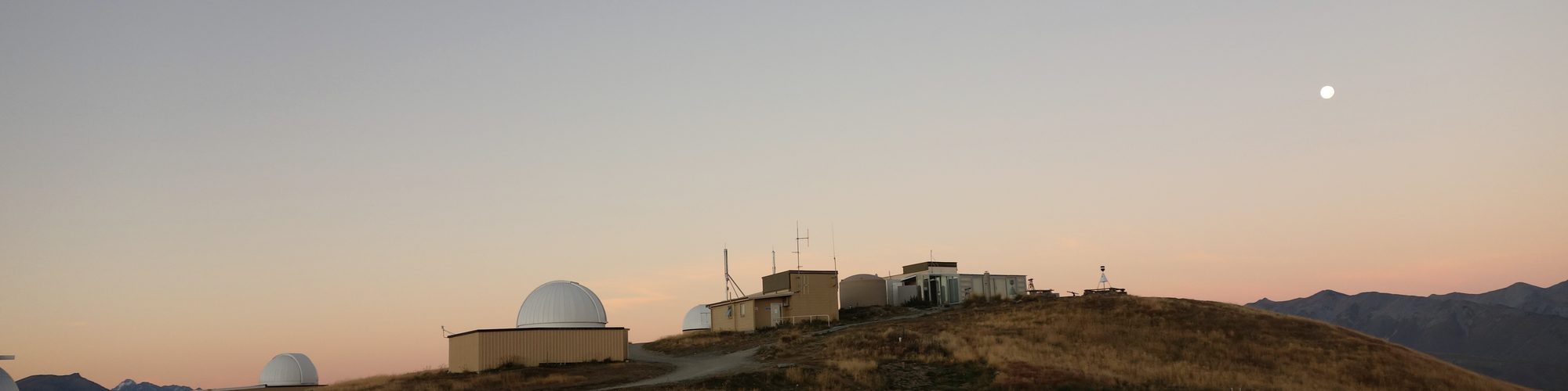 Observatory domes on a hilltop at dusk, with the moon rising: instruments that keep watching